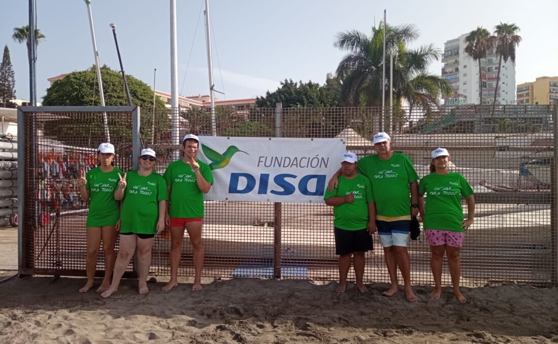 Seis participantes de Un mar para tod@s ante el cartel de Fundación DISA en Los Cristianos