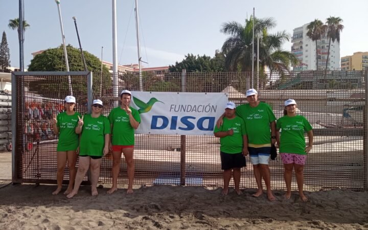 Seis participantes de Un mar para tod@s ante el cartel de Fundación DISA en Los Cristianos